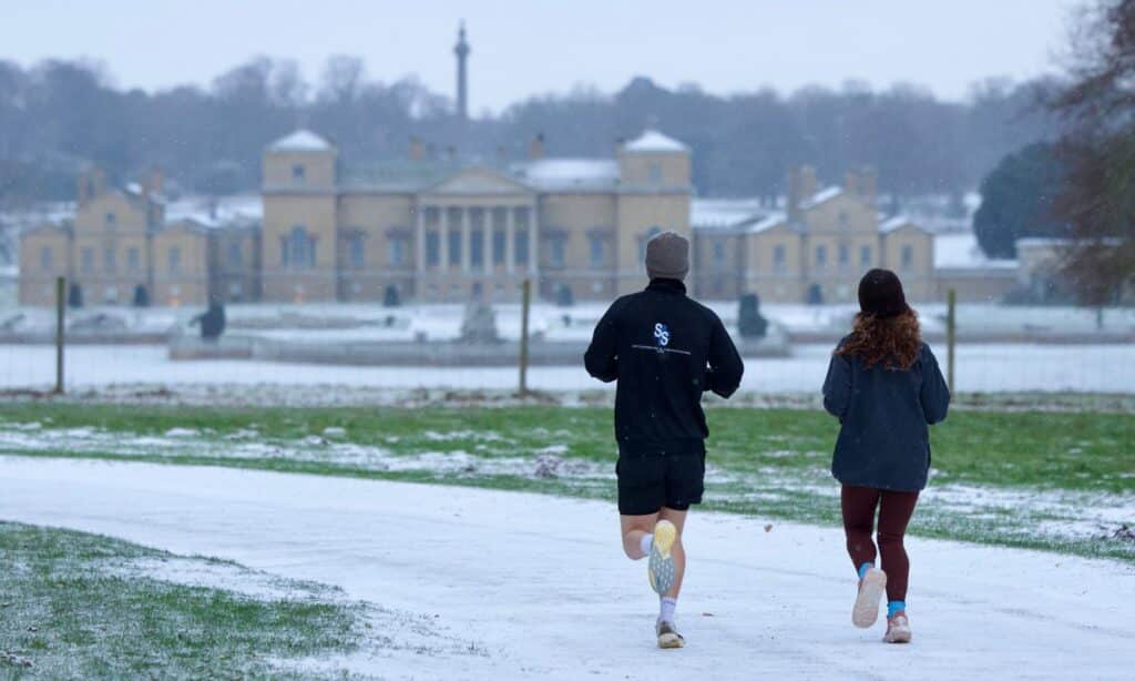 Two people running in snowy Holkham Park with Holkham Hall in the background.