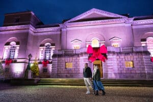 Two people walk in front of the North Side of Holkham Hall all decked from Christmas.
