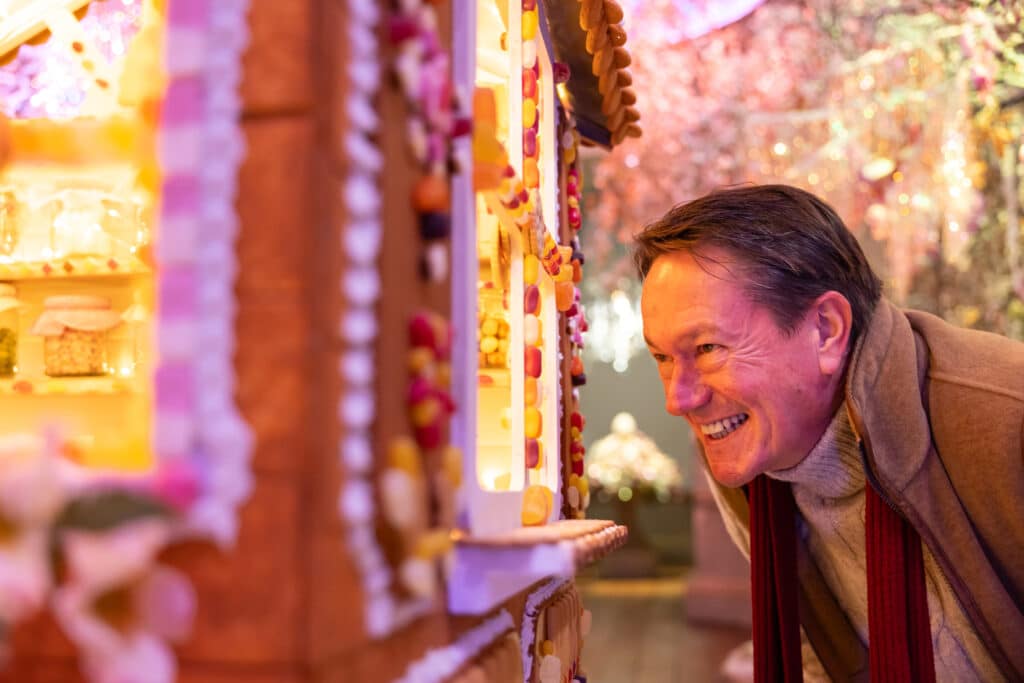 A man with dark hair smiles as he peeks inside a gingerbread house in the Statue Gallery at Holkham.
