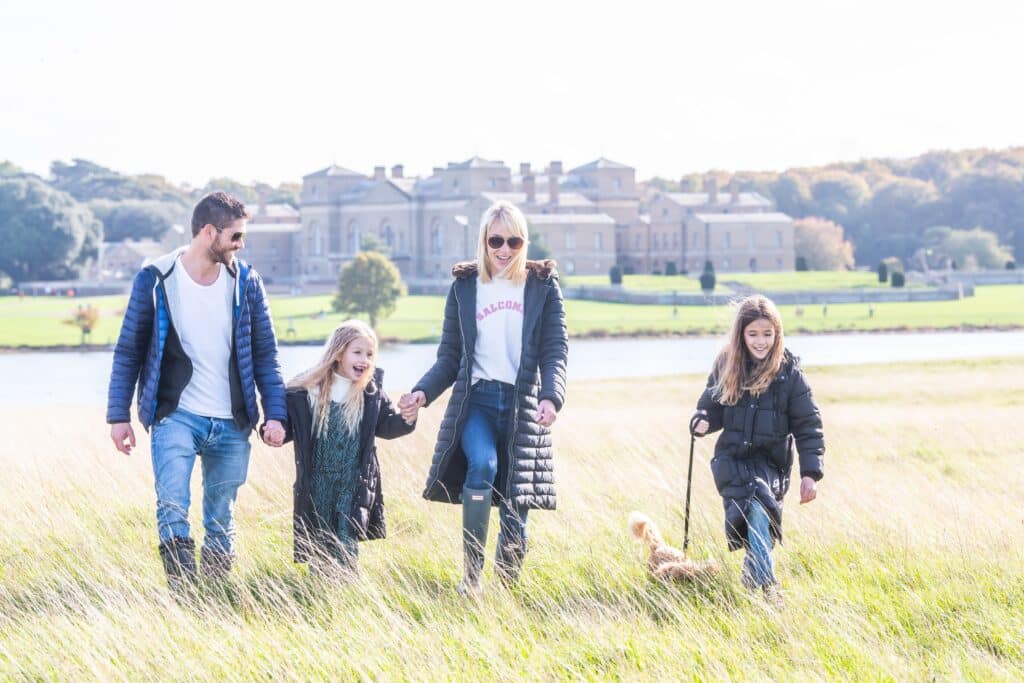 A family and their dog exploring Holkham park with the hall and lake in the background