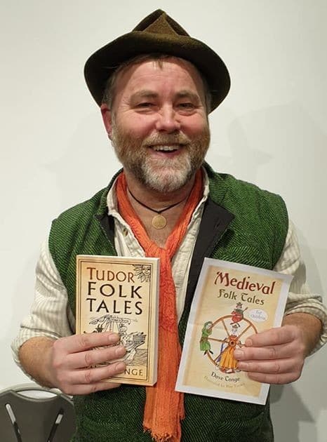 A man in a green jacket and hat holding two children's books