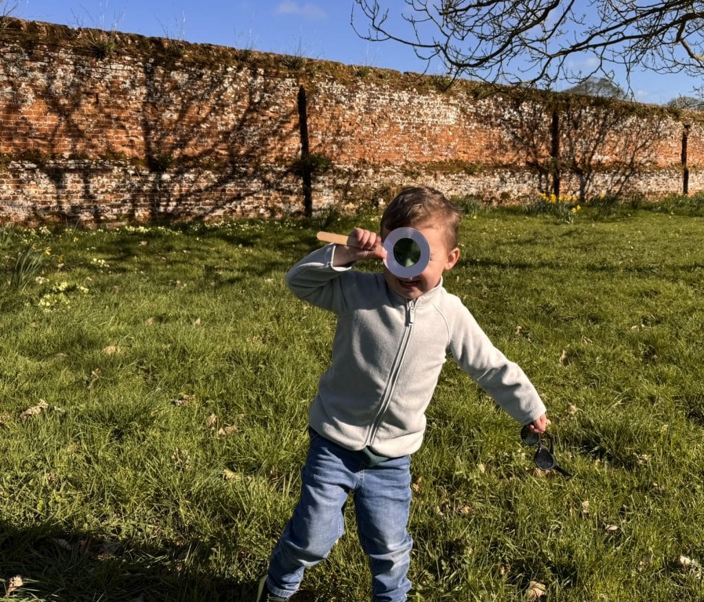 A boy holds a handmade magnifying glass outside the Walled Garden