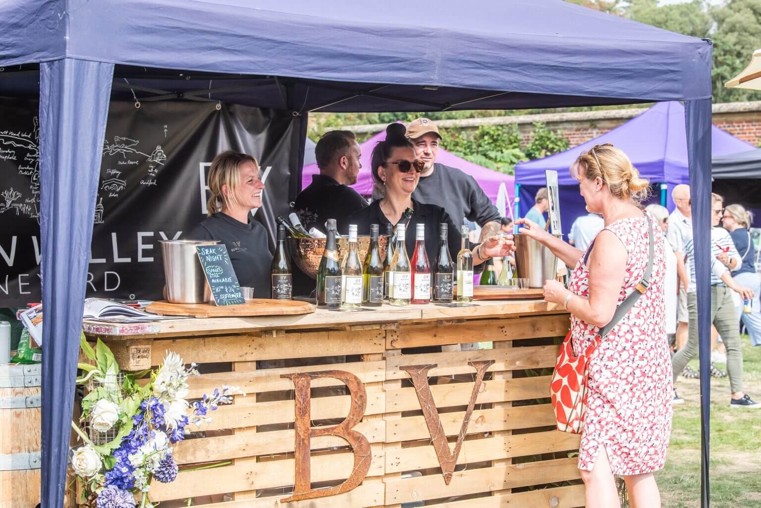 A woman buying drinks from a pop-up wooden bar at the North Norfolk Food & Drink Festival