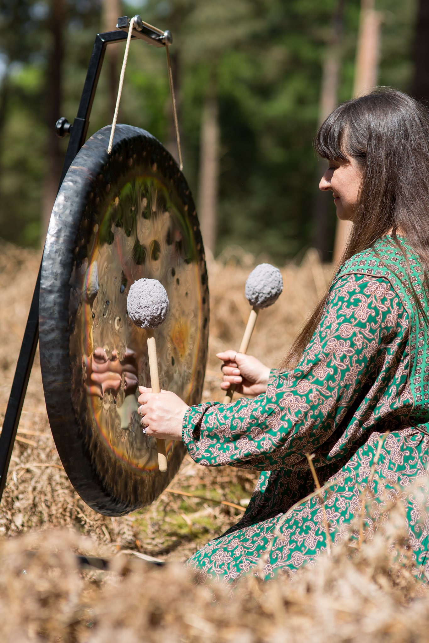 A woman plays a sound bath gong instrument in a forest
