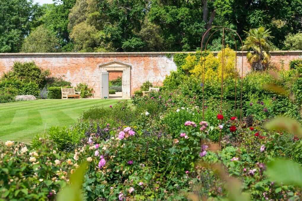 Plants and a stripy lawn in front of a archway in a wall in Holkham's Walled Garden