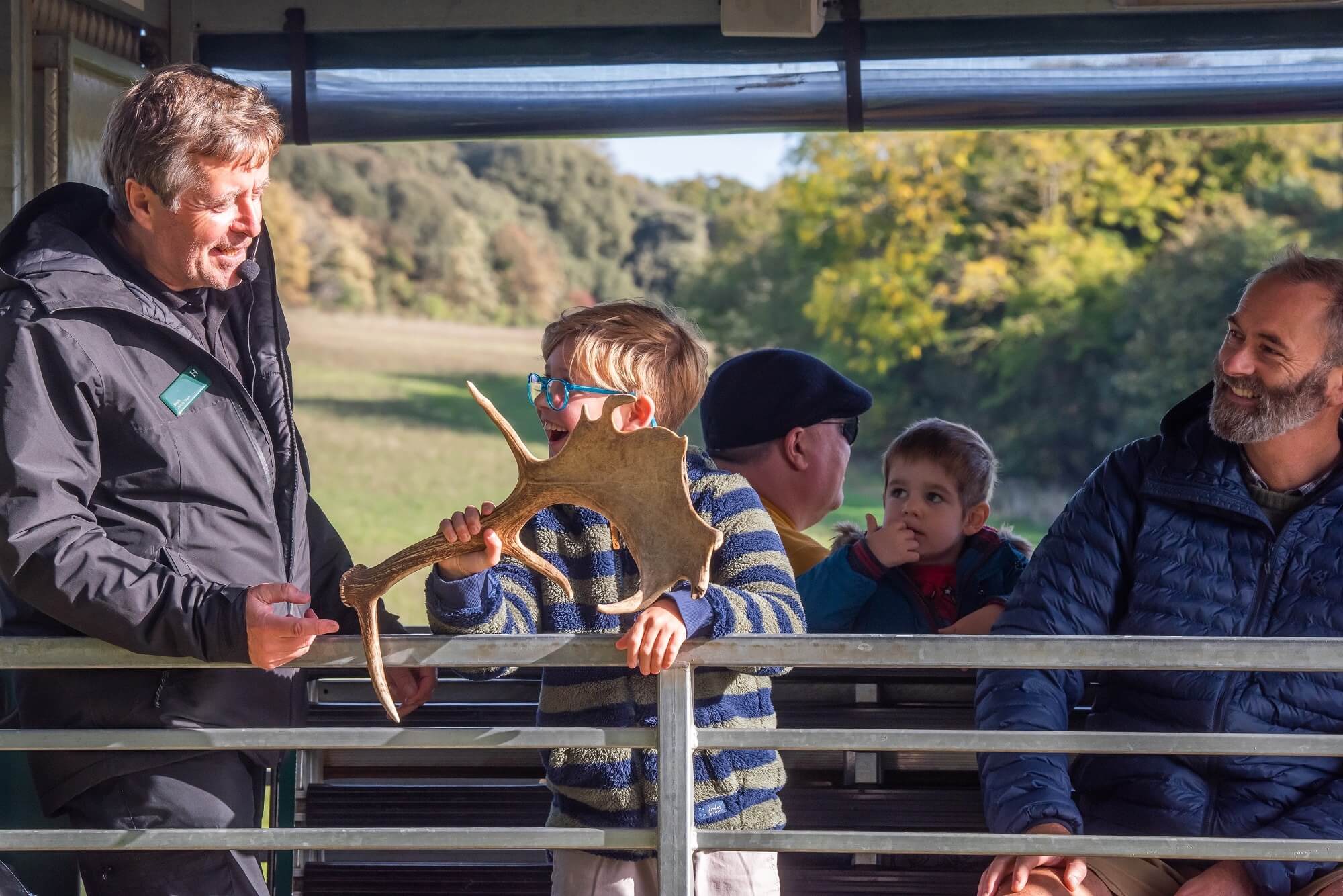 A boy holds a deer antler and chats with the tour guide on a tractor trailer