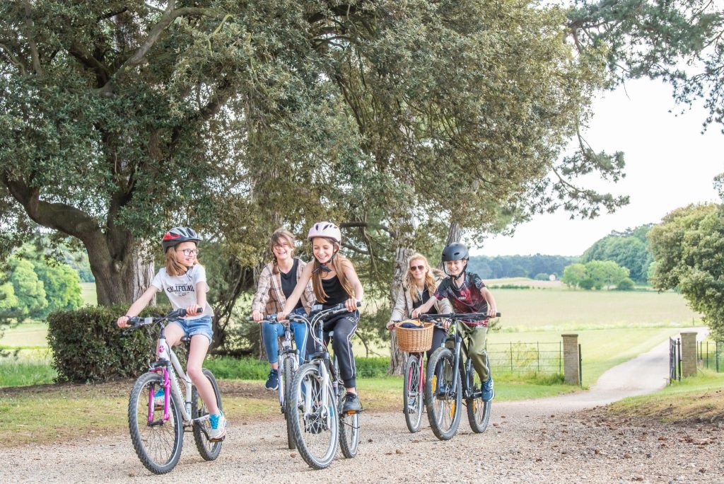 A group of children and adults cycle up a path at Holkham Park on a summer's day