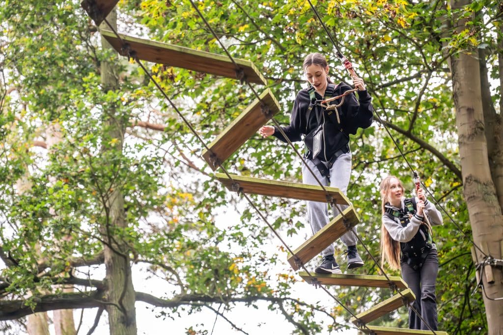Two teenagers cross zig zag wooden beams on the ropes course at Holkham