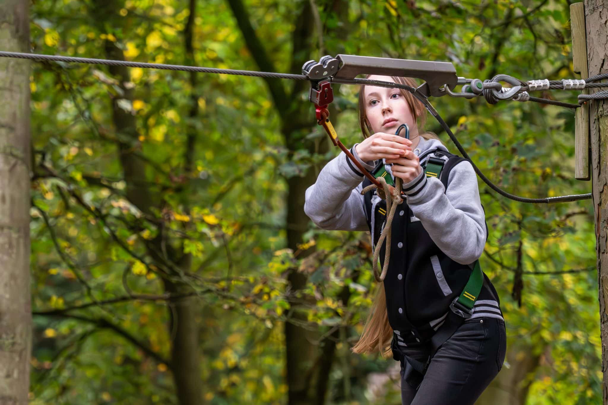 A teenage girl in a jacket and harness in the trees on the Holkham ropes course