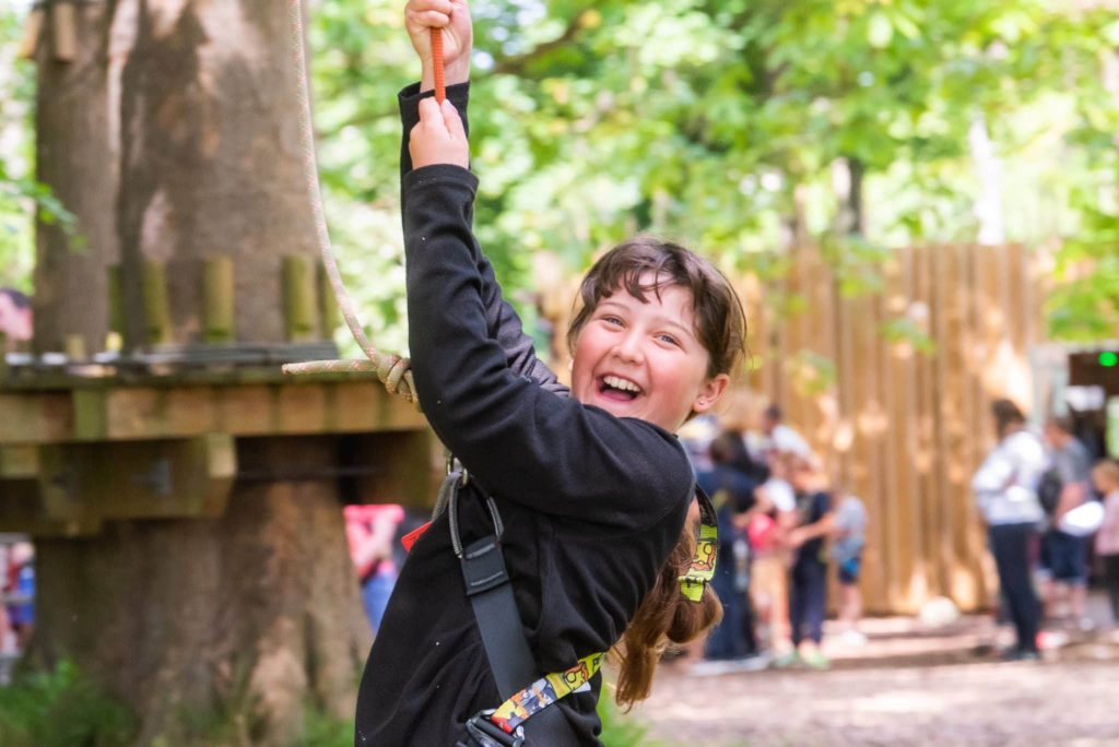 A girl in a harness beams while at the ropes course at Holkham