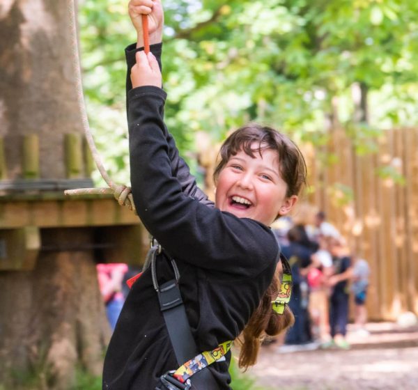 A girl in a harness beams while at the ropes course at Holkham