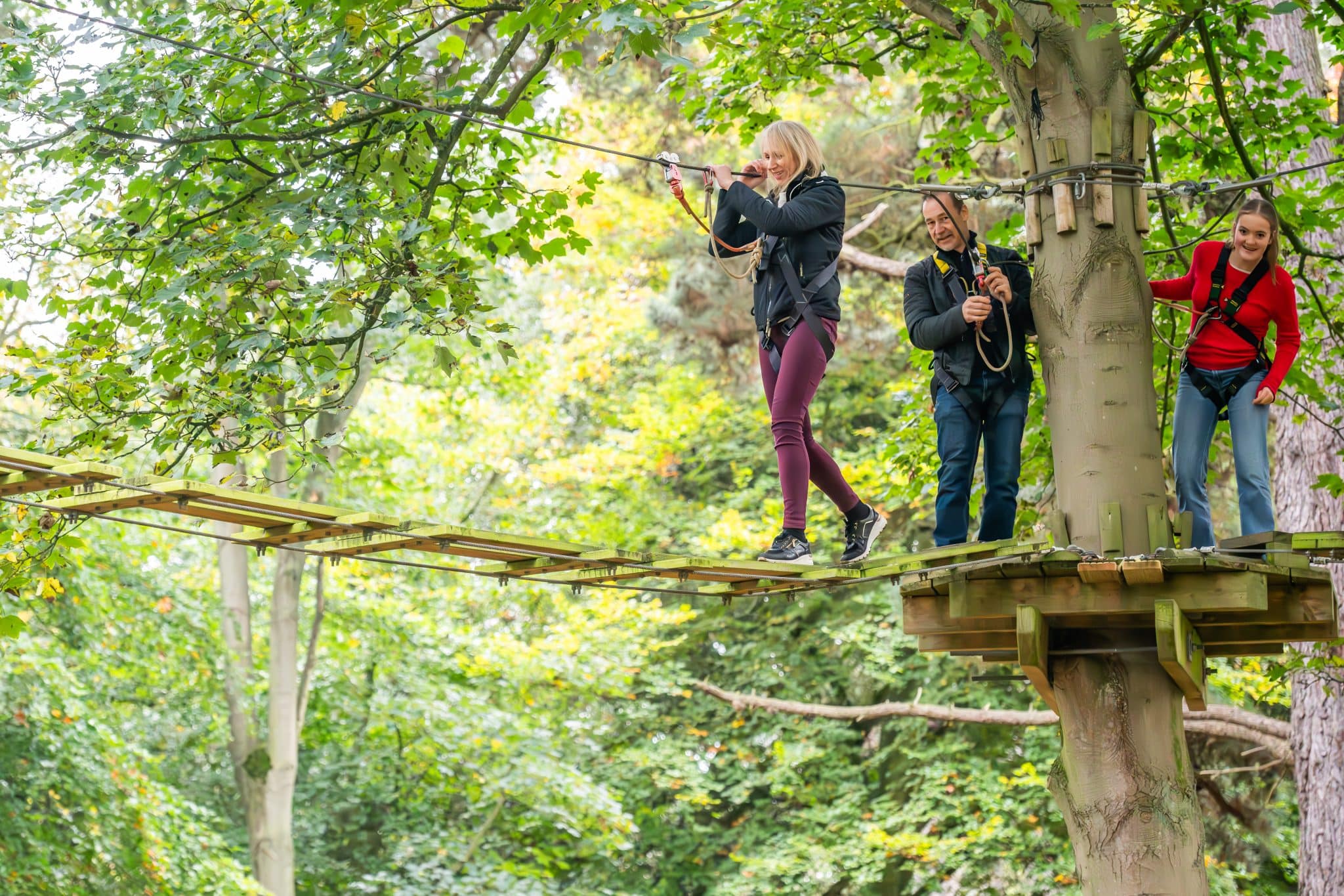 Two adults and a teenager in harnesses on the ropes course at Holkham