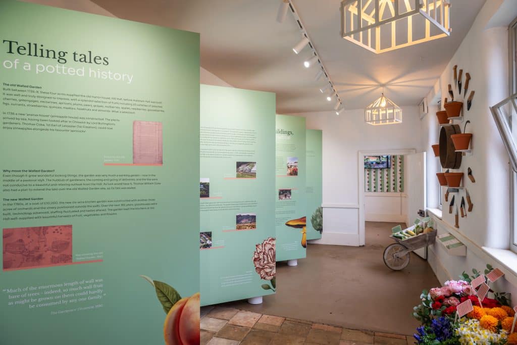 Green full height displays with text about Holkham Walled Garden and a wall display created using old garden tools in the Walled Garden Stories exhibition