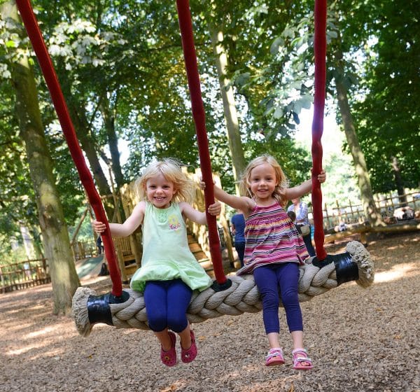 Two young girls grin on a large swing at Holkham Park