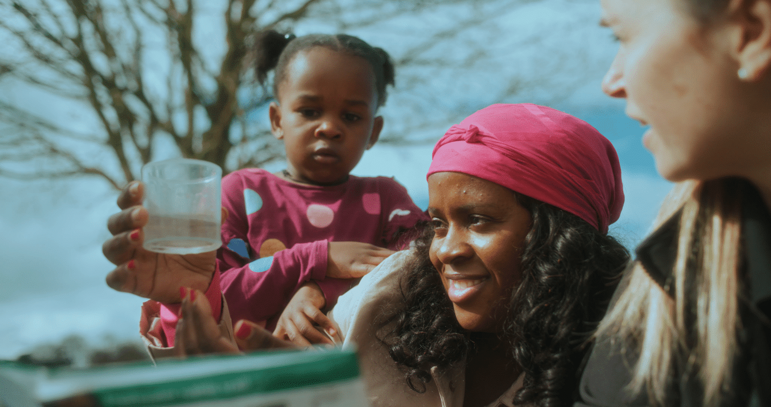 A mum and her daughter look into a pot of pond water while pond dipping at Holkham