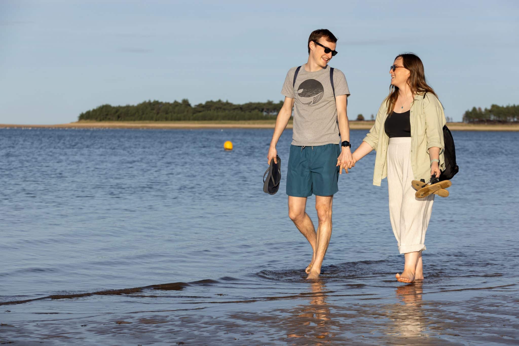 A couple in their 30s paddle in the sea hand in hand