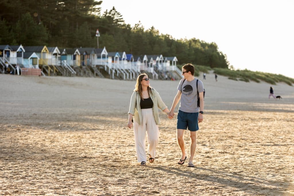 A couple in their 30s walk along Wells Beach at sunset