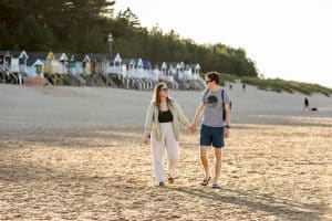 A couple in their 30s walk along Wells Beach at sunset