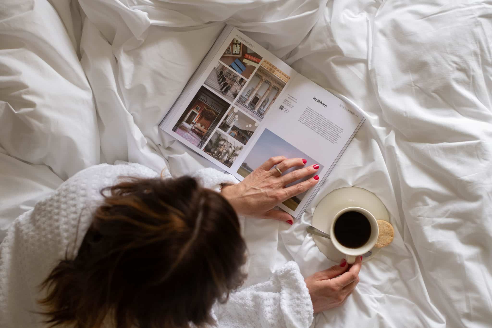 A woman relaxes on a bed with a coffee and magazine