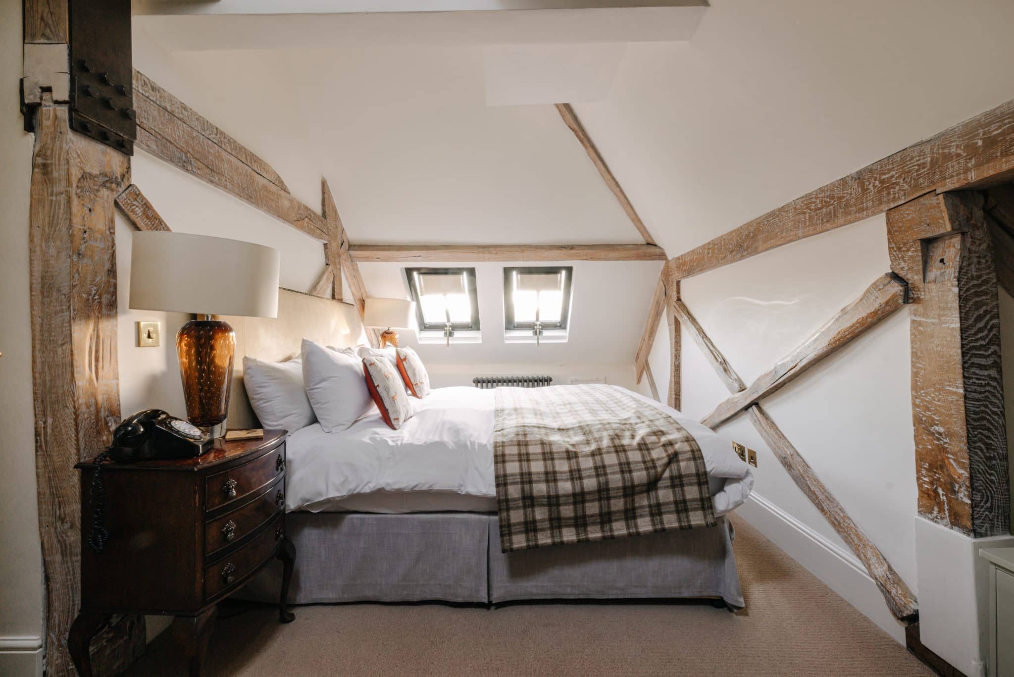 A bed in an attic room with sloping ceilings and beams.