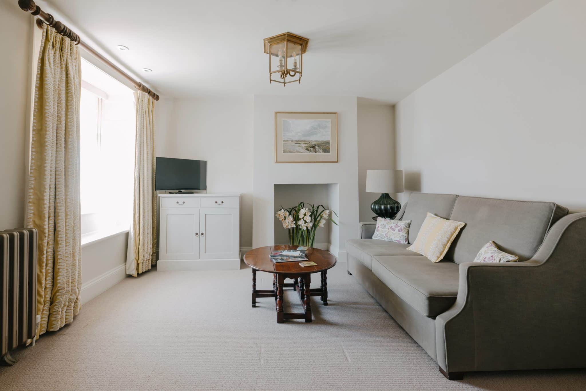 A light and airy lounge area in a hotel room with sofa, coffee table and TV.